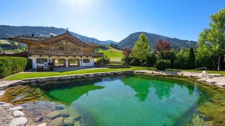 Großzügiger Gartenbereich mit Naturpool und Blick auf die umliegende Berglandschaft.