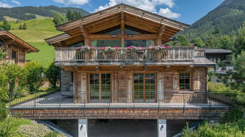 Traditionelles Holzchalet mit Balkonen und Bergblick, eingebettet in eine grüne Landschaft.