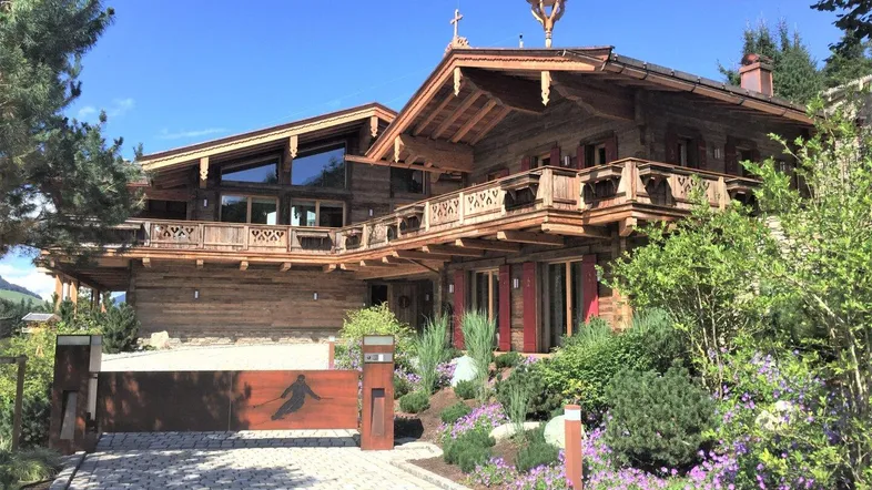Traditionelles Holzchalet mit aufwendigen Balkonen und gepflegtem Vorgarten unter blauem Himmel.