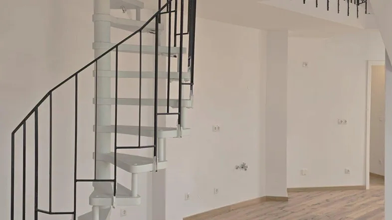Eine moderne weiße Wendeltreppe mit schwarzem Geländer in einem hellen, offenen Raum.