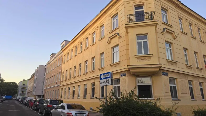 Gelbe Altbaufassade mit vielen Fenstern und einem kleinen französischen Balkon an der Ecke.