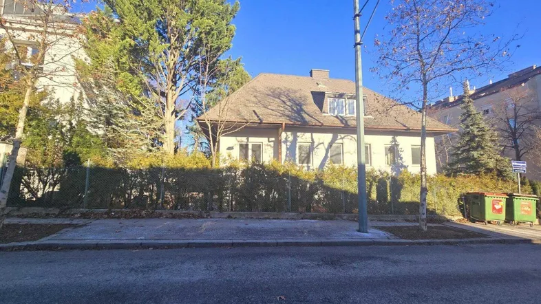 Einfamilienhaus mit Mansarddach und umgebender Hecke von der Straße aus gesehen.