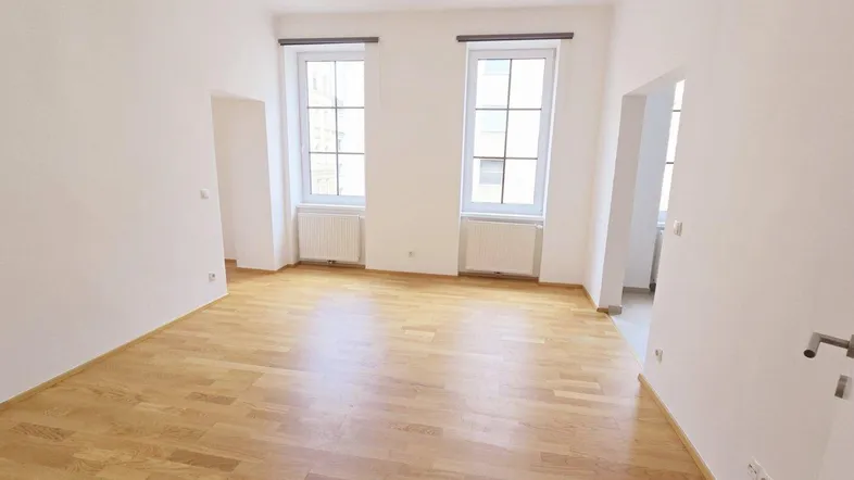 Helles, leeres Zimmer mit Parkettboden, weißen Wänden und zwei Fenstern, bereit zur individuellen Gestaltung.
