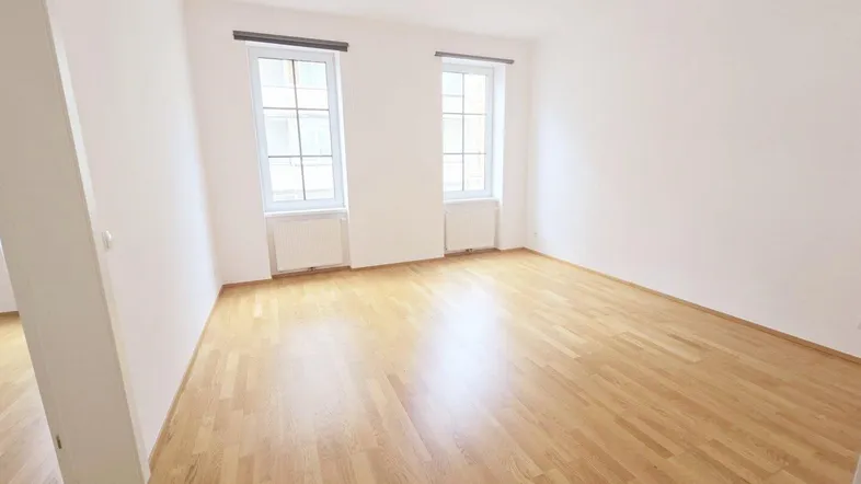 Helles Zimmer mit Parkettboden und zwei Fenstern, ideal als Wohn- oder Schlafzimmer nutzbar.