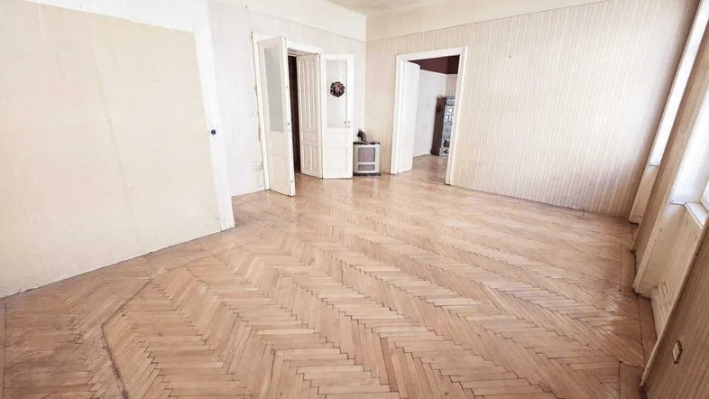 Geräumiges Zimmer mit Fischgrätparkettboden und hohen Fenstern, bereit für eine Renovierung.
