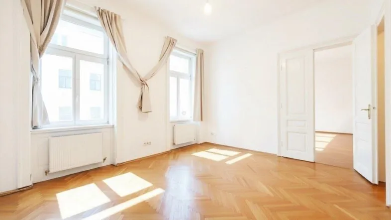Helles Zimmer mit Fischgrätparkett und großen Fenstern, das viel Tageslicht hereinlässt.