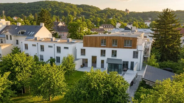 Moderne Wohnanlage mit weißer Fassade, Holzdetails und grüner Umgebung bei Sonnenuntergang.