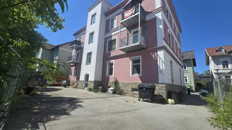 Mehrfamilienhaus mit rosa Fassade, weißen Akzenten und mehreren Balkonen unter blauem Himmel.