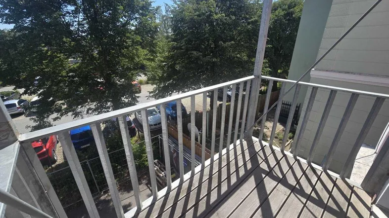 Balkon mit Holzfußboden und Metallgeländer, bietet einen Blick auf Bäume und parkende Autos.