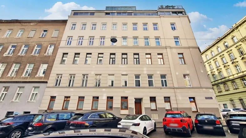 Fassade eines Mehrfamilienhauses mit parkenden Autos auf der Straße und Dachgeschossausbau.