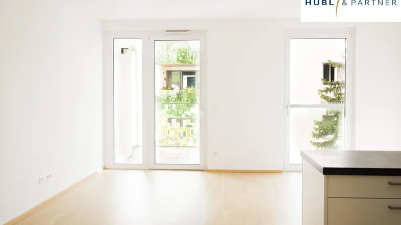 Helles, leeres Zimmer mit Parkettboden und Zugang zu einem Balkon, ideal als Wohnbereich.