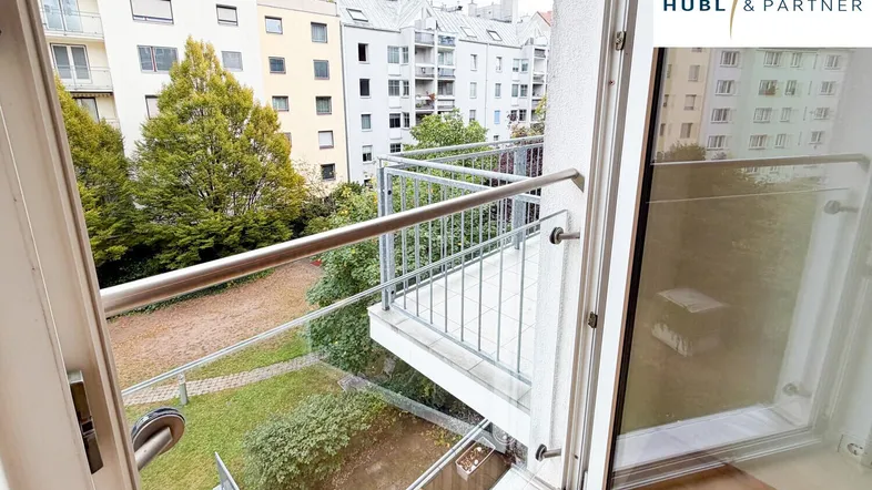 Balkon mit Metallgeländer und Blick auf den grünen Innenhof und die umliegenden Gebäude.