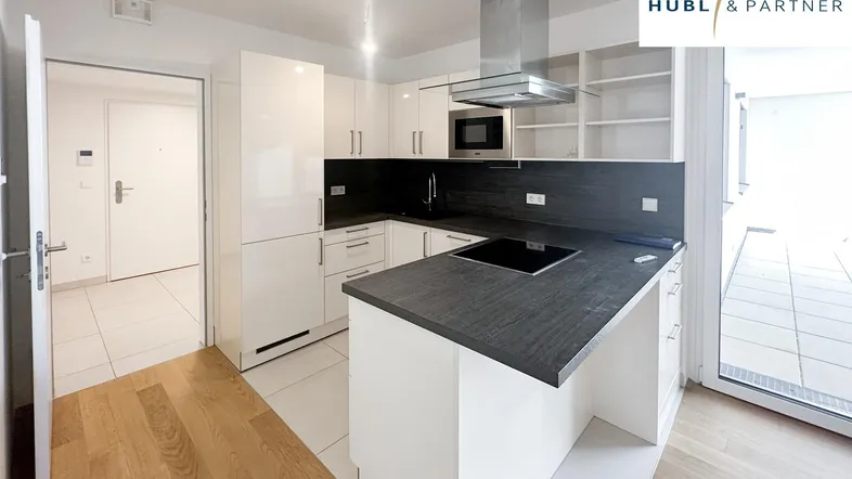 Moderne Einbauküche mit weißen Schränken, dunkler Arbeitsplatte und Holzboden, offen zum Wohnbereich.