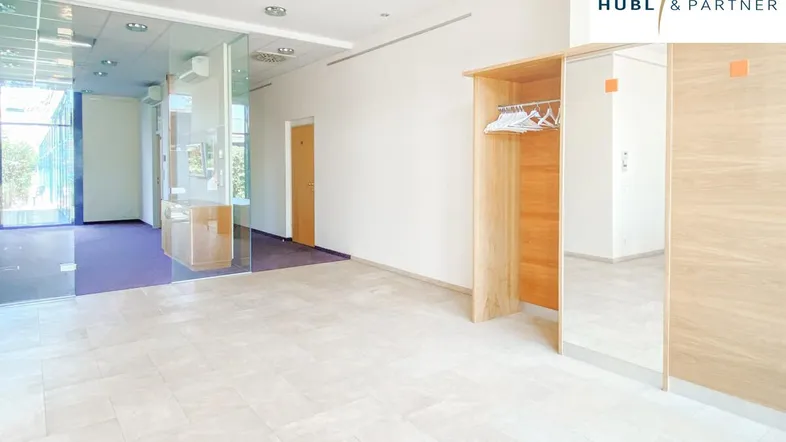 Geräumiger Empfangsbereich mit hellen Fliesen, Holzelementen und einer Garderobe, die zu weiteren Büroräumen führt.
