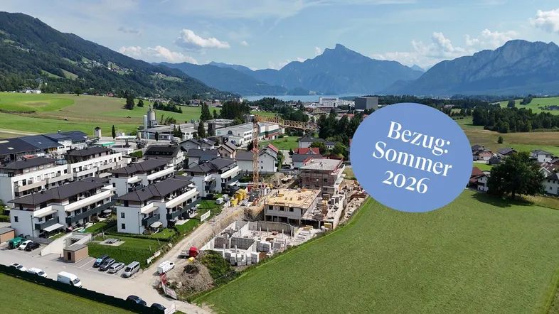 Luftaufnahme einer Neubausiedlung im Bau mit Berg- und Seeblick im Hintergrund.