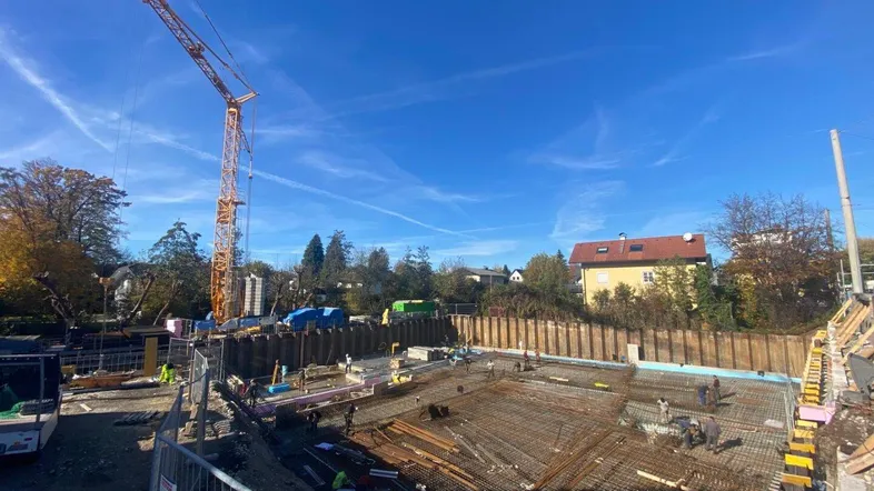 Baustelle mit Fundamentarbeiten, Bewehrung und Kran unter blauem Himmel.