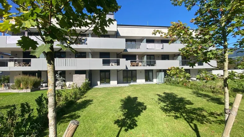 Modernes Mehrfamilienhaus mit Balkonen und gepflegter Rasenfläche unter blauem Himmel.