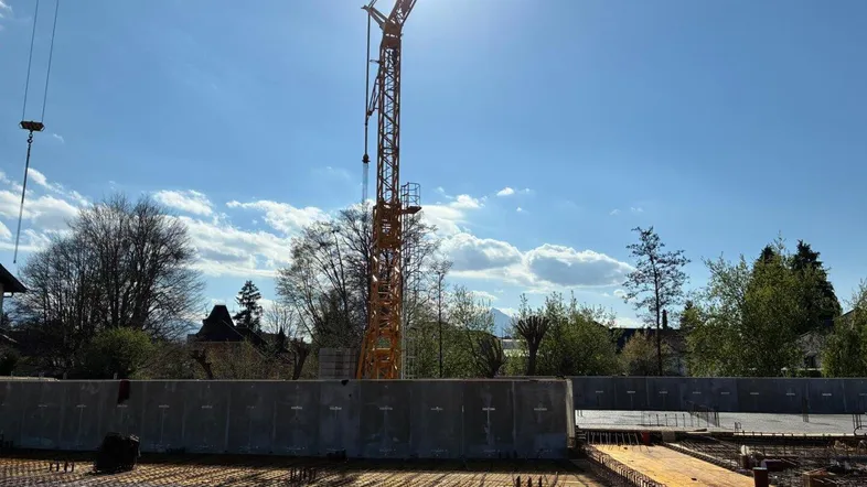 Baustelle mit Kran und vorbereiteter Fundamentplatte unter strahlendem Himmel und Sonnenschein.