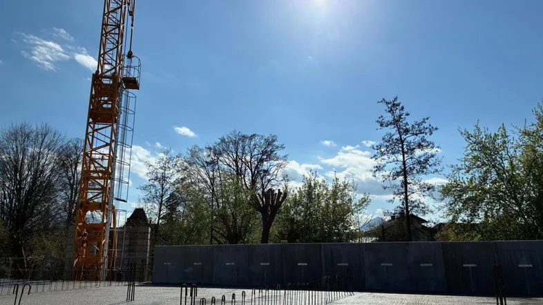 Baustelle bei sonnigem Wetter mit Kran und vorbereitetem Fundament für ein neues Gebäude.