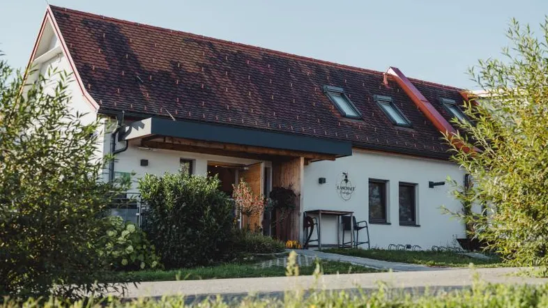 Modernes Gebäude mit Ziegeldach und Holzelementen, umgeben von grüner Landschaft.