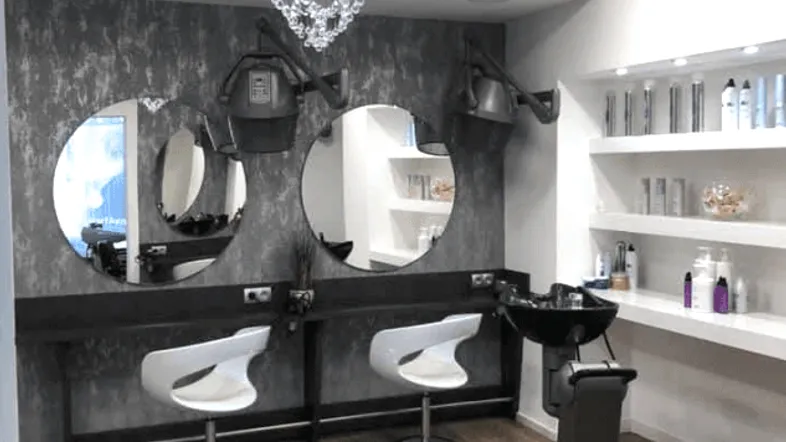 Moderner Friseursalon mit mehreren Styling-Stationen, Waschbecken und Produktregalen in stilvollem Ambiente.