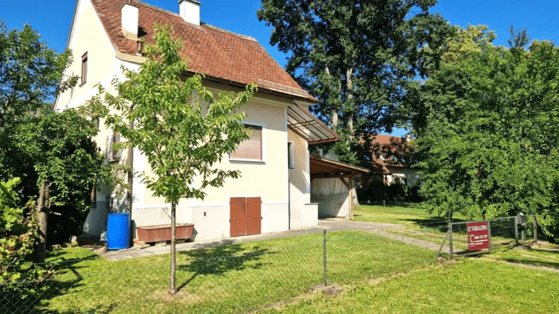 Freistehendes Haus mit Garten und Carport in ländlicher Umgebung unter blauem Himmel.