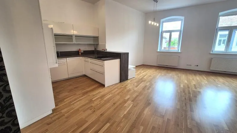 Heller offener Wohn-Essbereich mit moderner Einbauküche, Holzboden und großen Fenstern.