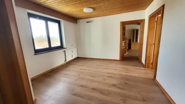 Helles Zimmer mit Holzbalkendecke und neuem Laminatboden, bietet Zugang zu weiteren Räumen.