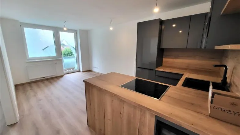 Moderne offene Küche mit Holzarbeitsplatten und integriertem Kochfeld, verbunden mit dem Wohnbereich und Balkonzugang.
