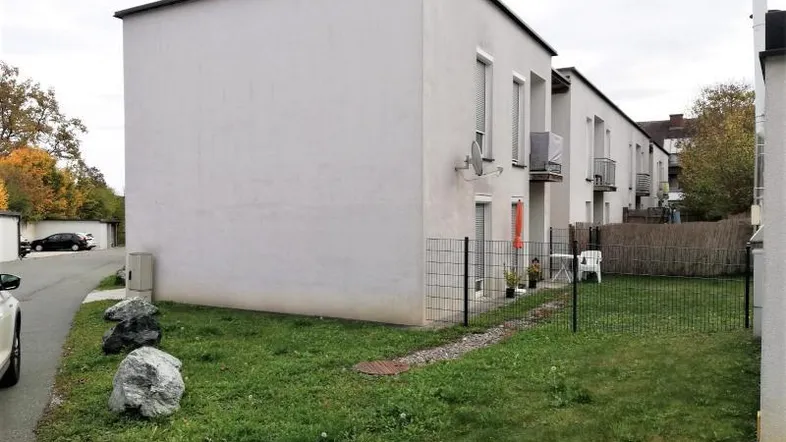 Seitenansicht eines Mehrfamilienhauses mit kleinem Gartenbereich und Balkonen.