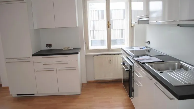 Moderne, helle Küche mit weißen Schränken, dunkler Arbeitsplatte und Fenster.