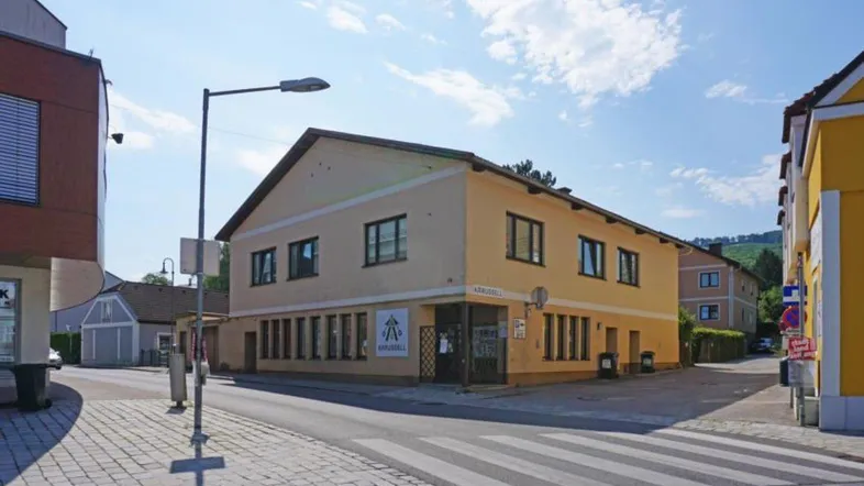 Gelbes Gebäude an einer Straßenecke mit Geschäften im Erdgeschoss und Wohnungen darüber.