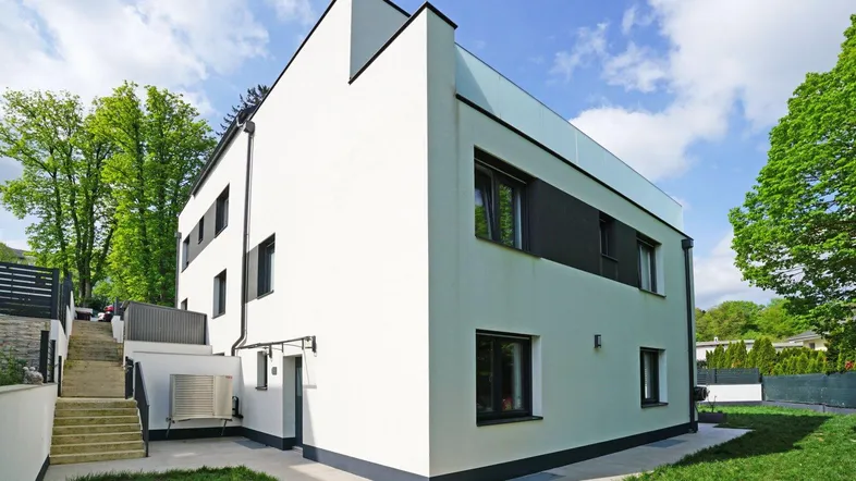 Modernes weißes Gebäude mit klaren Linien, schwarzen Fensterrahmen und einer Außentreppe.