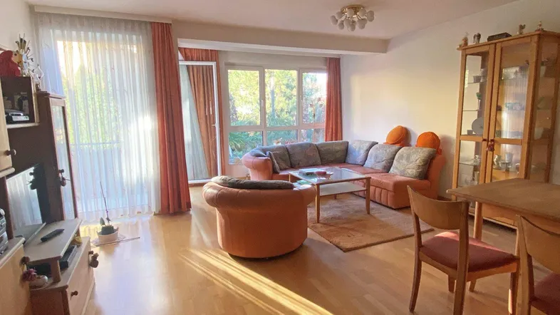Helles Wohn- und Esszimmer mit Parkettboden, großen Fenstern und Zugang zum Balkon.
