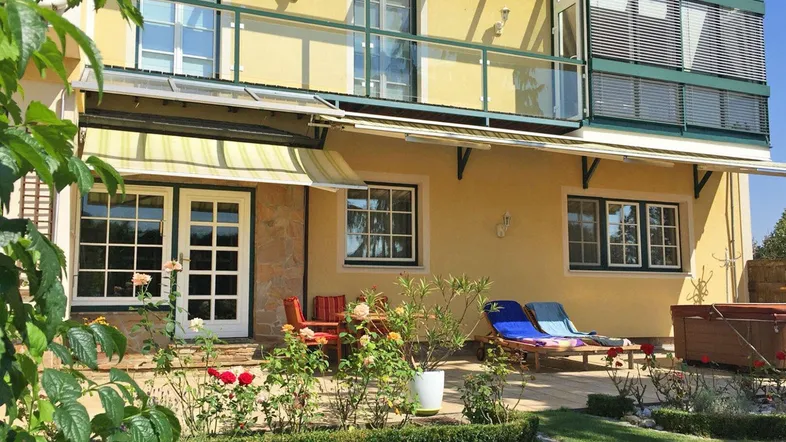 Gelbe Hausfassade mit möblierter Terrasse, Markise und gepflegtem Gartenbereich.