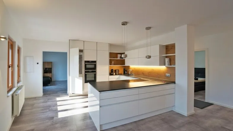 Moderne offene Küche mit Kochinsel, integrierten Geräten und viel Tageslicht.