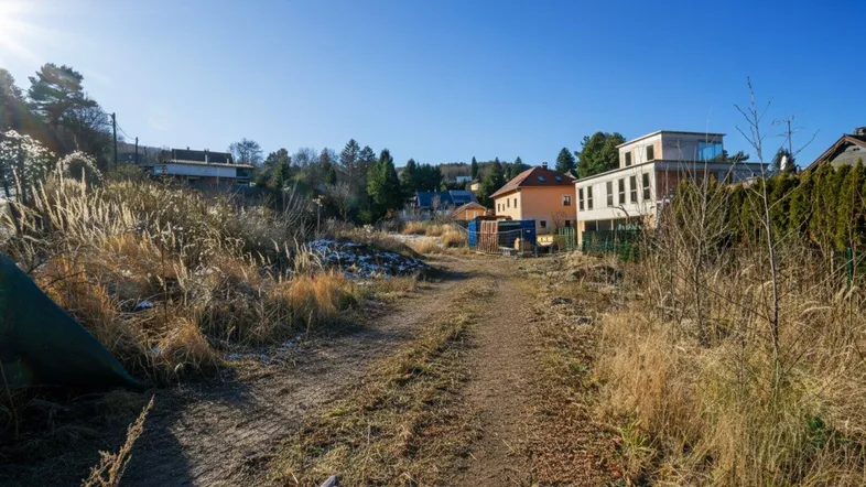 Unbefestigter Weg durch ein sonniges Grundstück mit umliegenden Wohnhäusern und viel Grün.