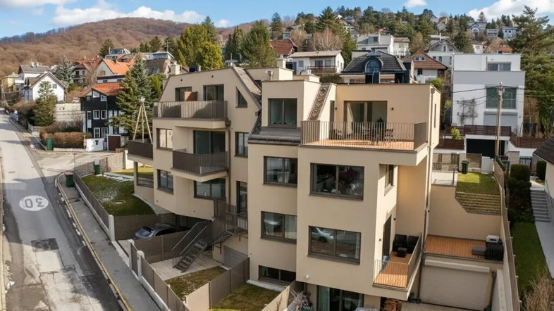Moderne Wohnanlage mit mehreren Balkonen und Terrassen in einer grünen Umgebung am Hang.