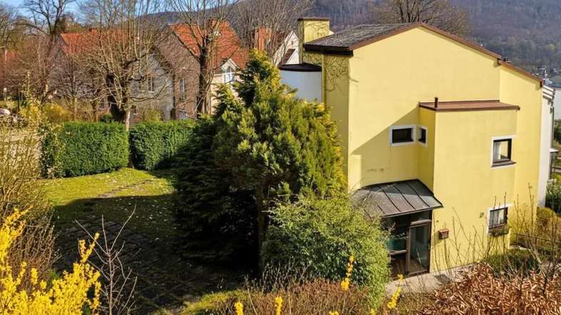 Gelbes Haus mit begrüntem Gartenbereich und Blick auf die umliegende Hügellandschaft.