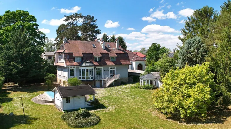 Großzügige Villa mit weitläufigem Garten, kleinem Pool, Gartenpavillon und Spielbereich unter blauem Himmel.