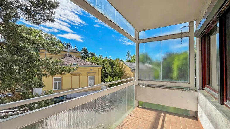 Geräumiger Balkon mit Fliesenboden und Blick ins Grüne sowie auf umliegende Gebäude.