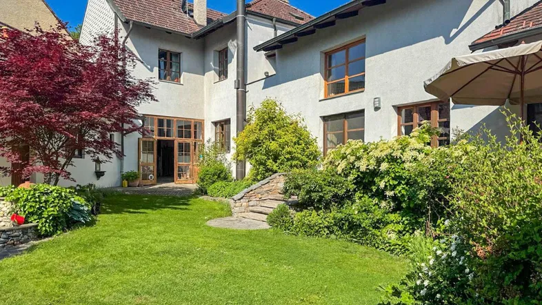 Gepflegter Gartenbereich mit Rasenfläche, üppiger Bepflanzung und Zugang zum Haus.