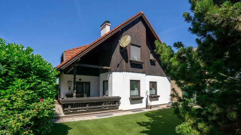 Traditionelles Haus mit dunkler Holzfassade und weißem Putz, umgeben von grünem Rasen und Büschen.
