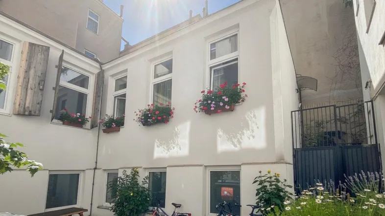 Heller Innenhof mit blühenden Blumenkästen an den Fenstern und Fahrrädern.