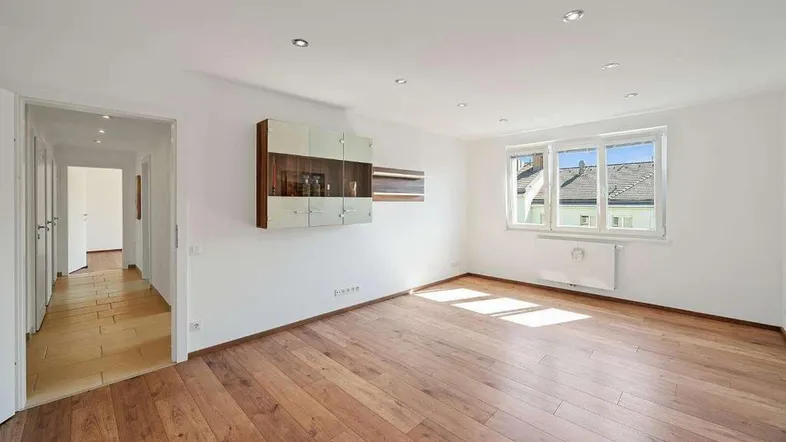 Helles Zimmer mit Holzboden, weißen Wänden und großem Fenster, ideal als Wohnzimmer.