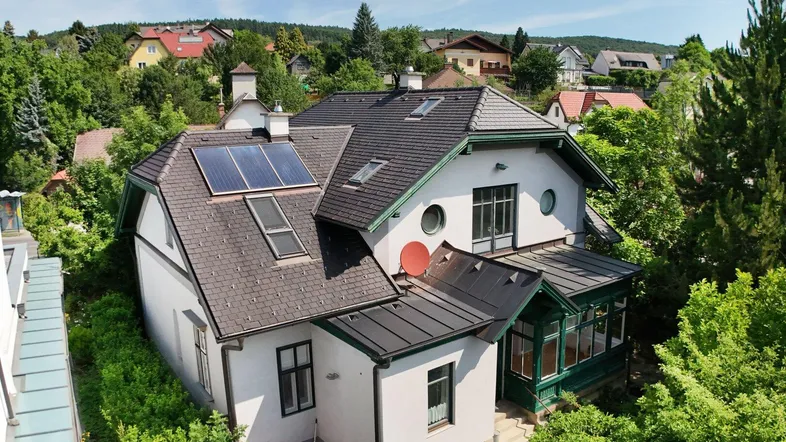 Hausansicht von oben mit Satteldach, Solarpaneelen und umgeben von viel Grün.