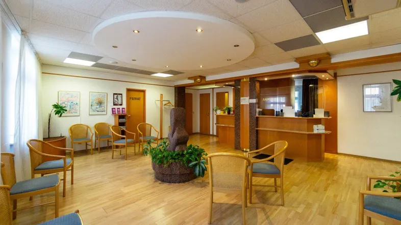 Geräumiger Wartebereich mit Holzfußboden, bequemen Stühlen und einer Rezeption für Patienten oder Kunden.