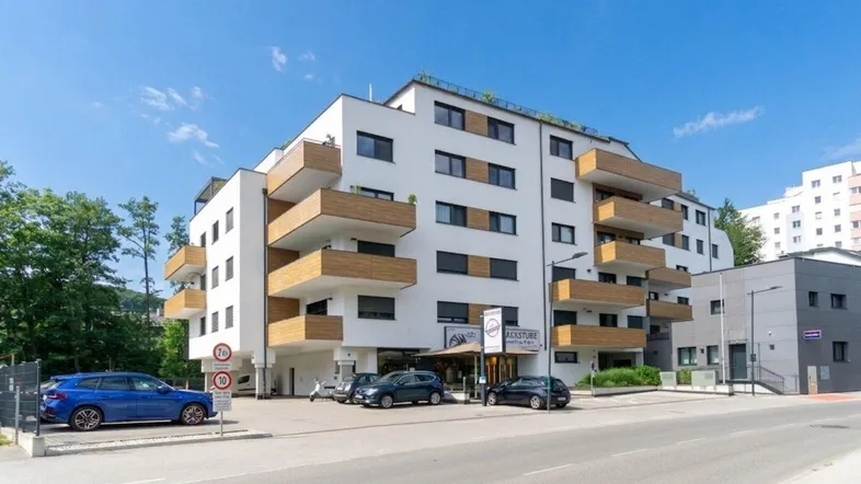 Modernes Mehrfamilienhaus mit weißer Fassade, Holzdetails und Balkonen an einer Straße gelegen.
