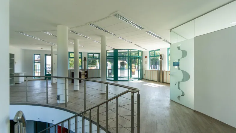 Heller, offener Bürobereich mit Säulen, großen Fenstern und einem Blick auf den Eingangsbereich.