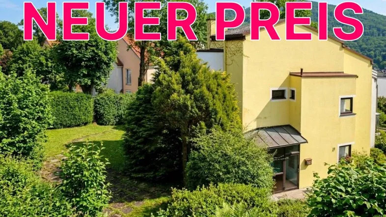 Gelbes Haus mit üppigem Garten, umgeben von Bäumen und Sträuchern, mit Bergblick im Hintergrund.